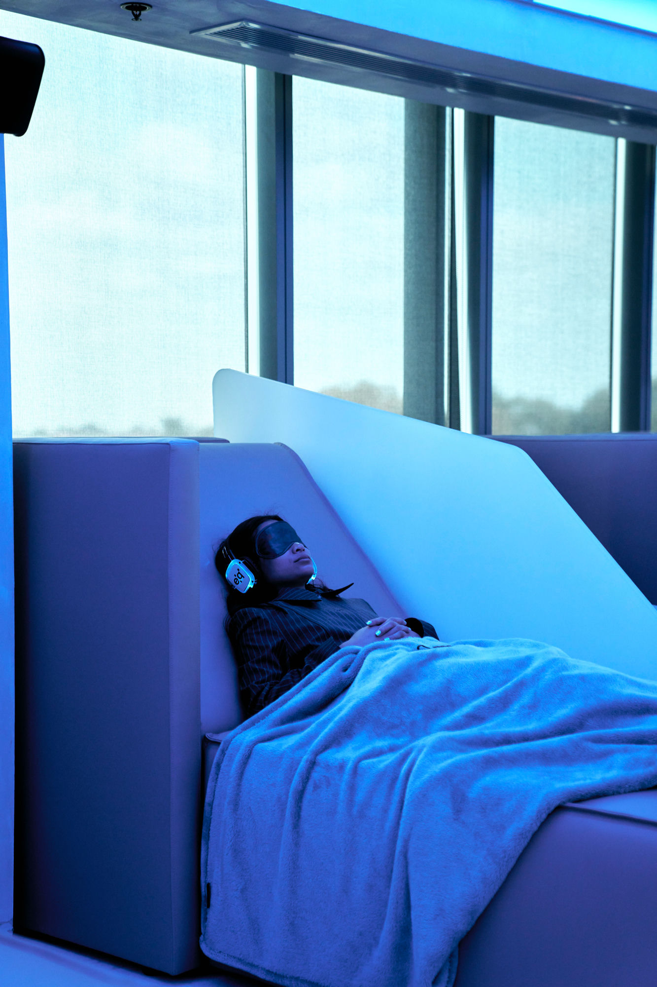 A guest resting under blue light with headphones and an eye mask