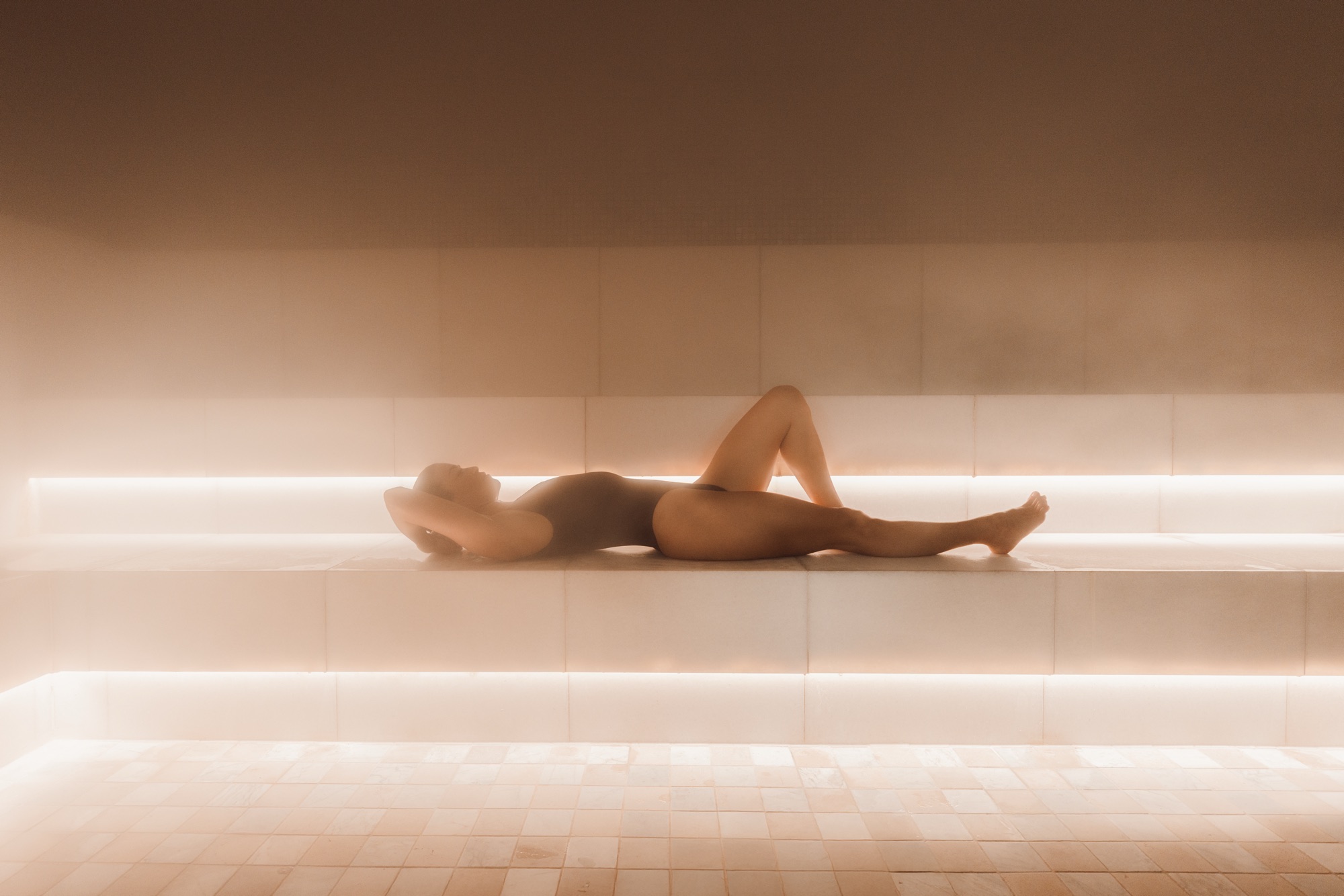 A guest lying back on a warm bench in the EQ Bathhouse